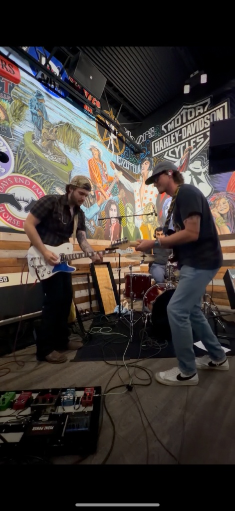 Chris and Danny playing guitar live in front of Harley Davidson mural