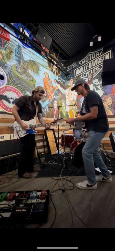 Chris and Danny facing off on guitars in front of Harley Davidson mural